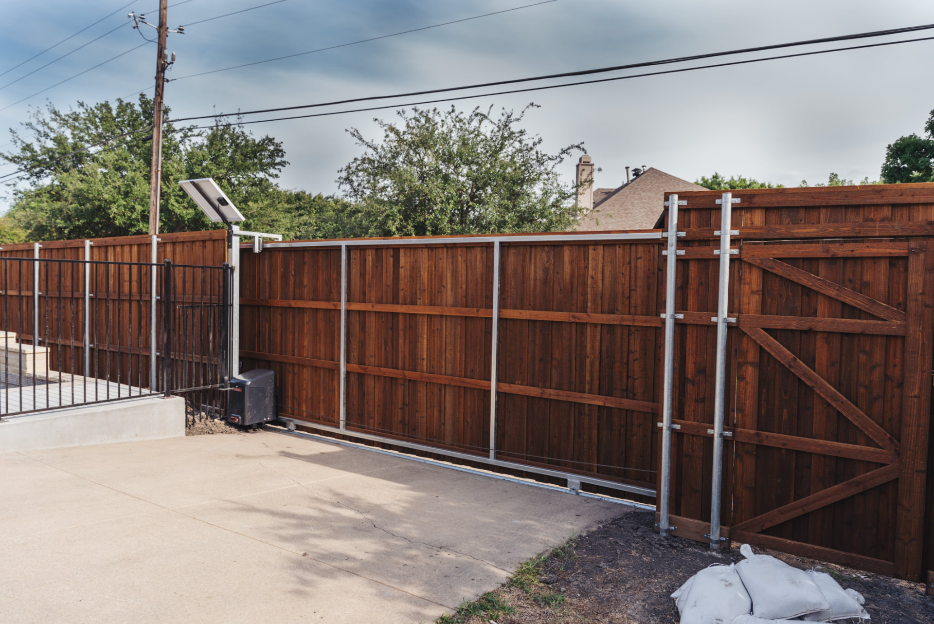 Cedar rolling driveway gate with solar operator and iron fence in Pearland TX